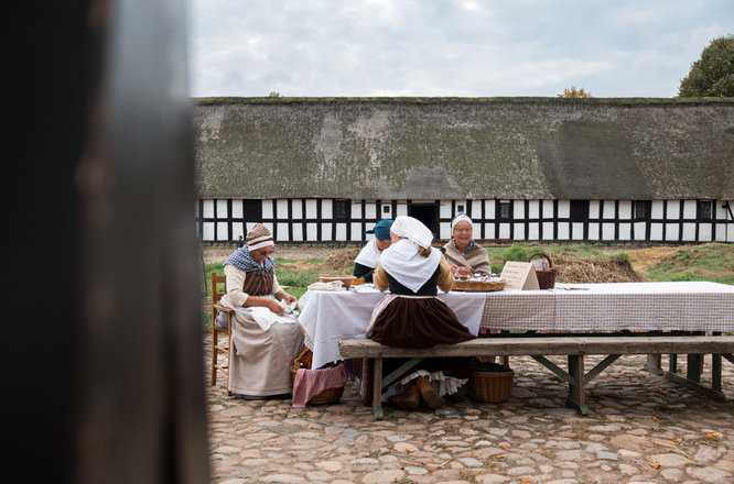 Kvinder i traditionelt tøj foran stor gård